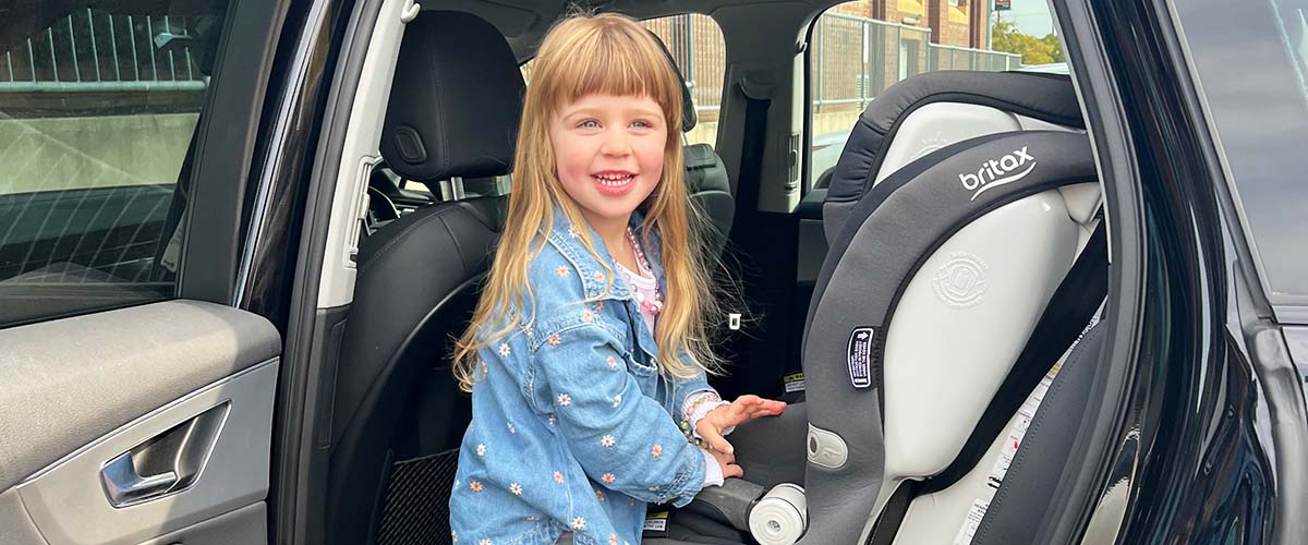 A girl standing next to a car seat