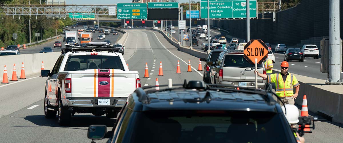 Roadworker is holding a "Slow" sign on the road.