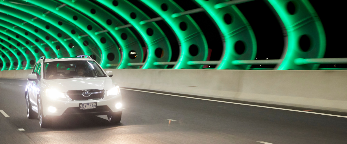 White car drives through the Sound Tube on CityLink which is lit up green.
