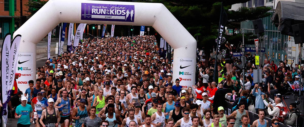 Runners at the start of a running race under a large banner that says Run for the Kids.